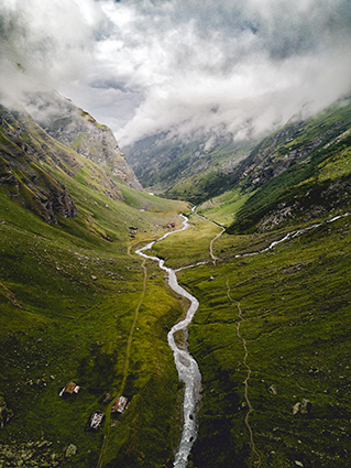 A photo taken from above of a river flowing and twisting through a valley of green lush mountains