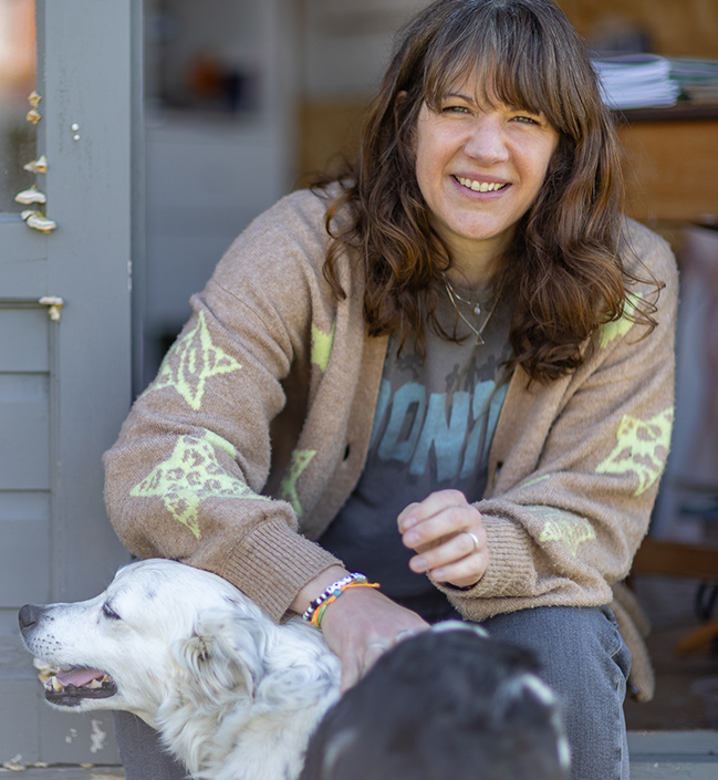 A photo of Sara Truckel sat in the doorway to her studio with her dog