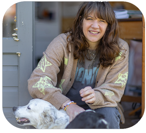 A phot of Sara Truckel with her border collie sat in the dorway to her studio