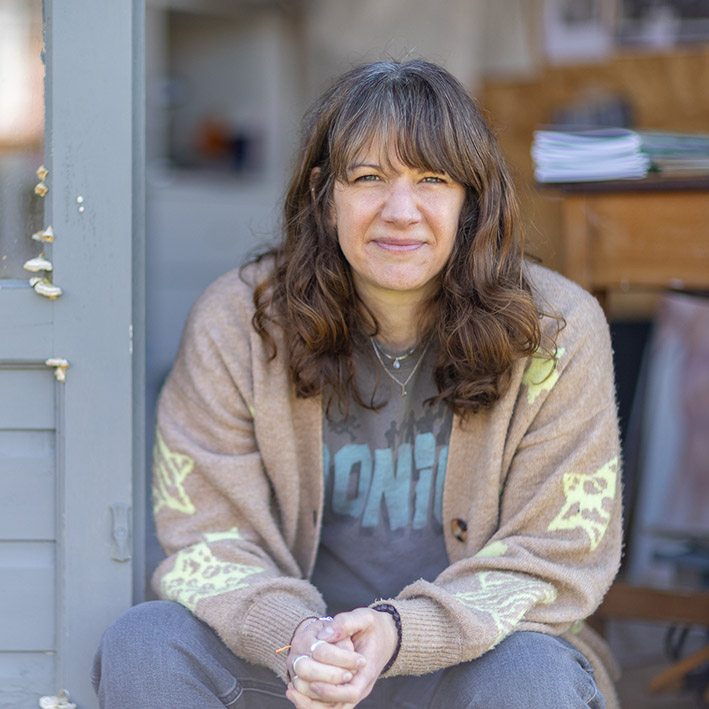 A photo of Sara Truckel, the Brand and Marketing Activist sat on the step of her art studio